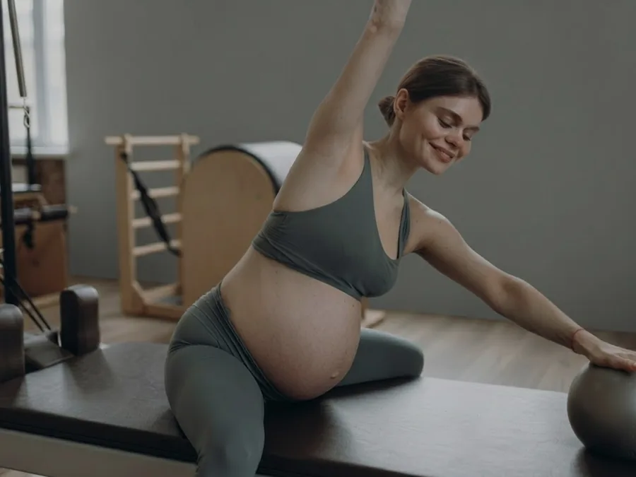 Alumna embarazada estirando con un fitball durante una clase de pilates
